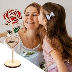 a mother and daughter kissing each other in front of a wooden rose with the word mama written on it