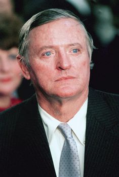 a man in a suit and tie looking off into the distance with people behind him