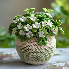 a crocheted planter with white and green flowers in it sitting on a table