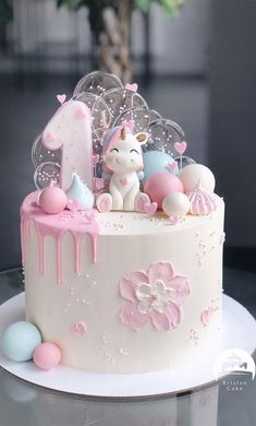 a white cake with pink icing and an unicorn figure on top is sitting on a table