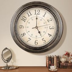 a large clock on the wall above a table with books and other items in front of it