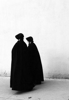 two people in black cloaks sitting on the ground looking at something off to the side