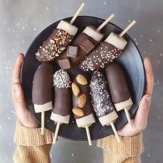 a person holding a black plate with chocolates and almonds on it in their hands