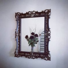 there is a vase with flowers in it on the wall mirror reflecting an old staircase