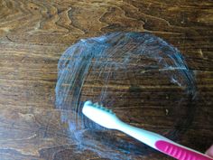 a pink toothbrush sitting on top of a wooden table next to a piece of plastic