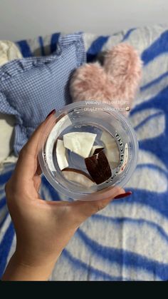 a person holding a plastic cup with some food in it on top of a bed