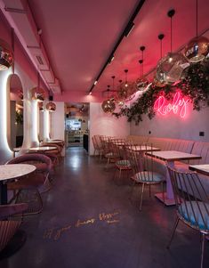 the interior of a restaurant with pink lighting and wooden tables, chairs, and hanging plants