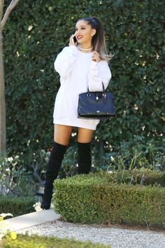 a woman is talking on her cell phone while wearing boots and a white sweater dress