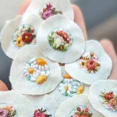 a person holding several small white flowers in their hands with embroidered designs on the petals