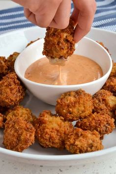 a person dipping something into a bowl of sauce on top of some fried meat patties