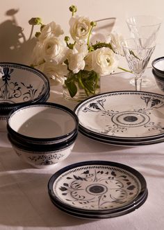 a table topped with black and white plates next to a glass vase filled with flowers