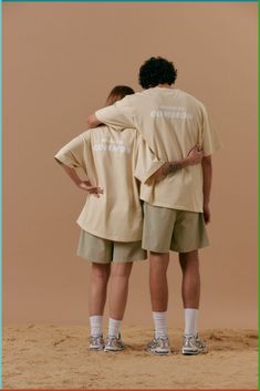 two people standing back to back with their arms around each other in front of a beige background