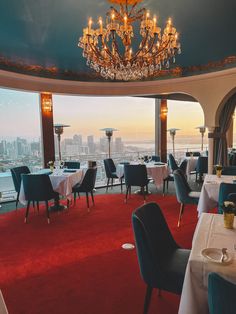 a dining room with chandelier and tables overlooking the cityscape at sunset