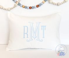 a white pillow with a blue monogrammed letter on it and beaded necklaces hanging from the wall