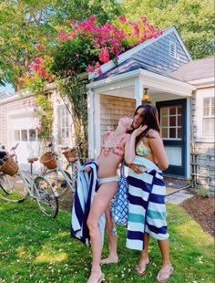 two women in bathing suits are standing by a house and some bicycles on the grass