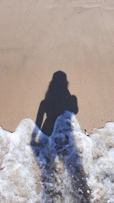 the shadow of a person standing on top of snow covered ground next to an ocean