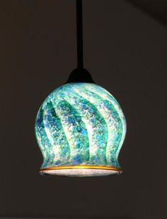 a green and blue glass light hanging from a black ceiling fixture in a room with white walls