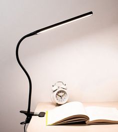 an open book is sitting on a desk next to a light that has a clock on it