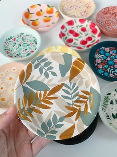 a hand is holding a paper plate in front of several plates with designs on them