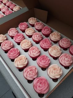 a box filled with pink cupcakes covered in frosting and rosettes on top