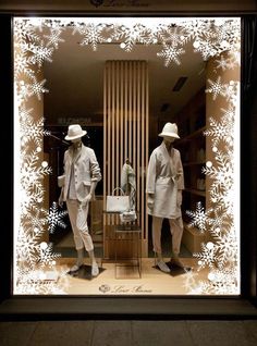 two mannequins dressed in suits and hats standing behind a display window with snowflakes on it