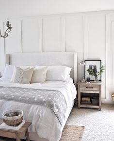 a bed with white linens and pillows in a bedroom next to a wooden table