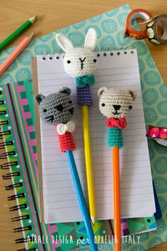 two crocheted animals on top of pencils in front of a notepad