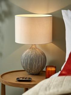 a table with a lamp on it and a remote control sitting next to the bed