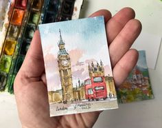 a hand holding up a small card with a painting of big ben in the background