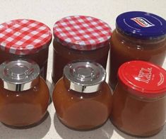 four jars of peanut butter are lined up on the counter top, one has a red and white checkered lid