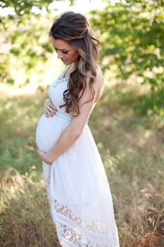 a pregnant woman is standing in the grass with her belly tucked under her stomach and wearing a white dress