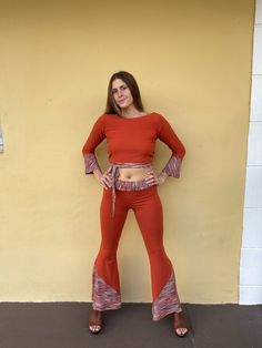 a woman standing in front of a yellow wall with her hands on her hips and wearing red pants