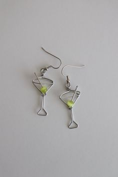 Martini Glass Earrings. Great gift for Bartenders, Hostesses and Waitresses. Tiny wire martini glasses, complete with green cat's eye bead. Surgical steel hooks are hypo-allergenic. Clear plastic stoppers on backs. Aluminum wire will not tarnish. I have been making custom wire art and jewelry for 30 years. I started in 1989 selling jewelry on the streets of Montreal. Over the years I have participated in many craft shows, exhibitions and sold my work in gallery shops across Canada including the Party Glass Jewelry Wire Wrapped, Party Wire Wrapped Glass Jewelry, Silver Wire-wrapped Earrings For Party, Silver Wire Wrapped Earrings For Party, Silver Glass Earrings For Party, Martini Olive, Cocktail Earrings, Wire Jewelry Designs, Diy Wire Jewelry