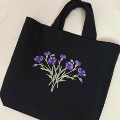 a black tote bag with purple flowers embroidered on the front and side, sitting on a white surface