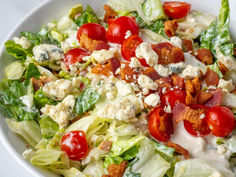 a salad with tomatoes, lettuce, bacon and dressing in a white bowl