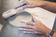 a person is working with clay on a potter's wheel while holding a knife