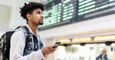 a man with dreadlocks is looking at his cell phone in an airport terminal