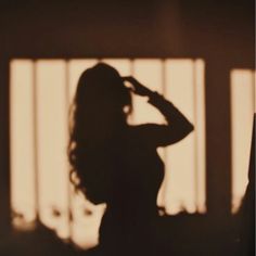 a woman standing in front of a window with her hand on her head and the sun shining through blinds behind her