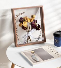 there is a coffee cup and some flowers on the table next to an open magazine