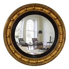 a round mirror reflecting a living room with chairs and a table in front of it