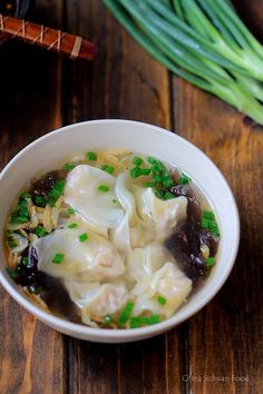 a white bowl filled with dumplings on top of a wooden table next to green onions