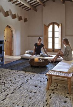 two women are sitting on the floor in a large room with windows and rugs