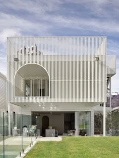 a white house that is next to a pool in the grass and surrounded by glass railings