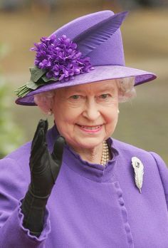 an older woman wearing a purple hat and holding her hand up to the side with a flower on it