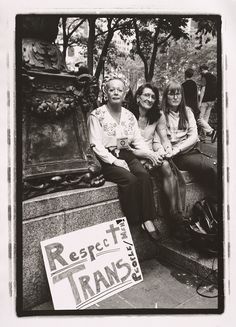 black and white photograph of three women sitting on a bench in front of a sign