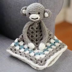 a crocheted monkey sitting on top of a gray couch next to a blue and white blanket