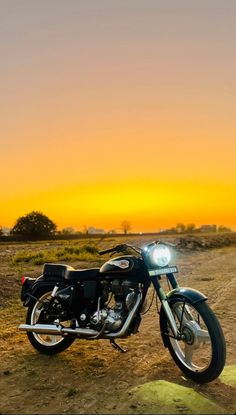 a motorcycle parked on the side of a dirt road in front of an orange sky