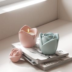 two pink and blue vases sitting on top of a magazine next to a candle