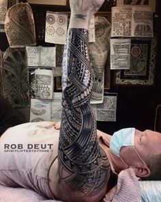 a man laying on top of a bed next to a wall covered in pictures and tattoos