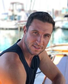 a man sitting on top of a boat next to the ocean with boats in the background